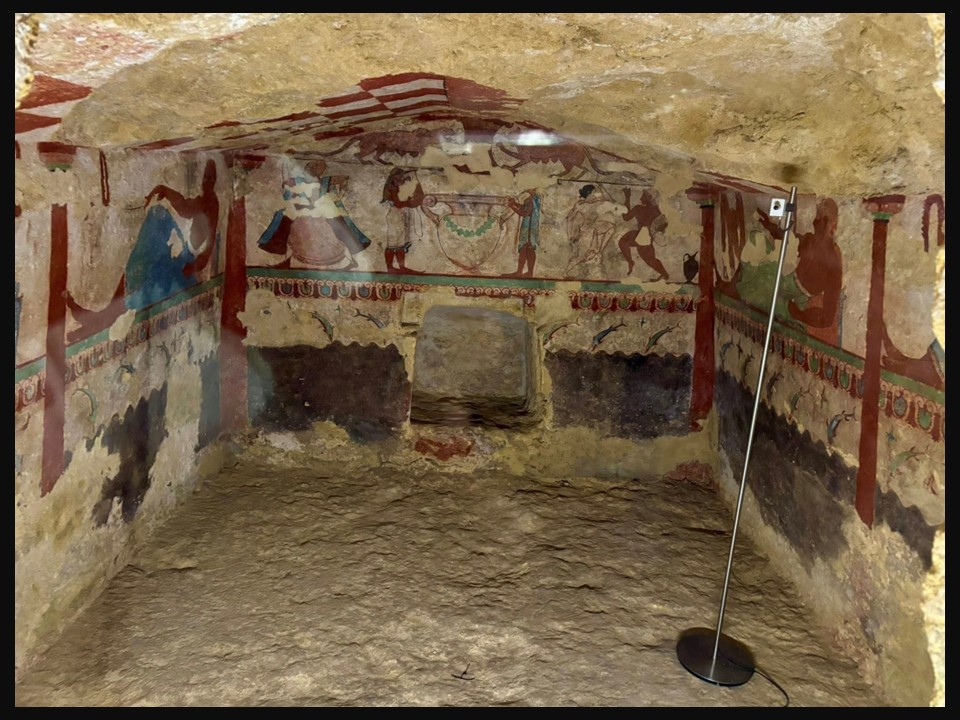 View of the interior of the Etruscan Tomb of the Lionesses showing frescoes of dancers, musicians, and a banquet scene beneath two facing lionesses.