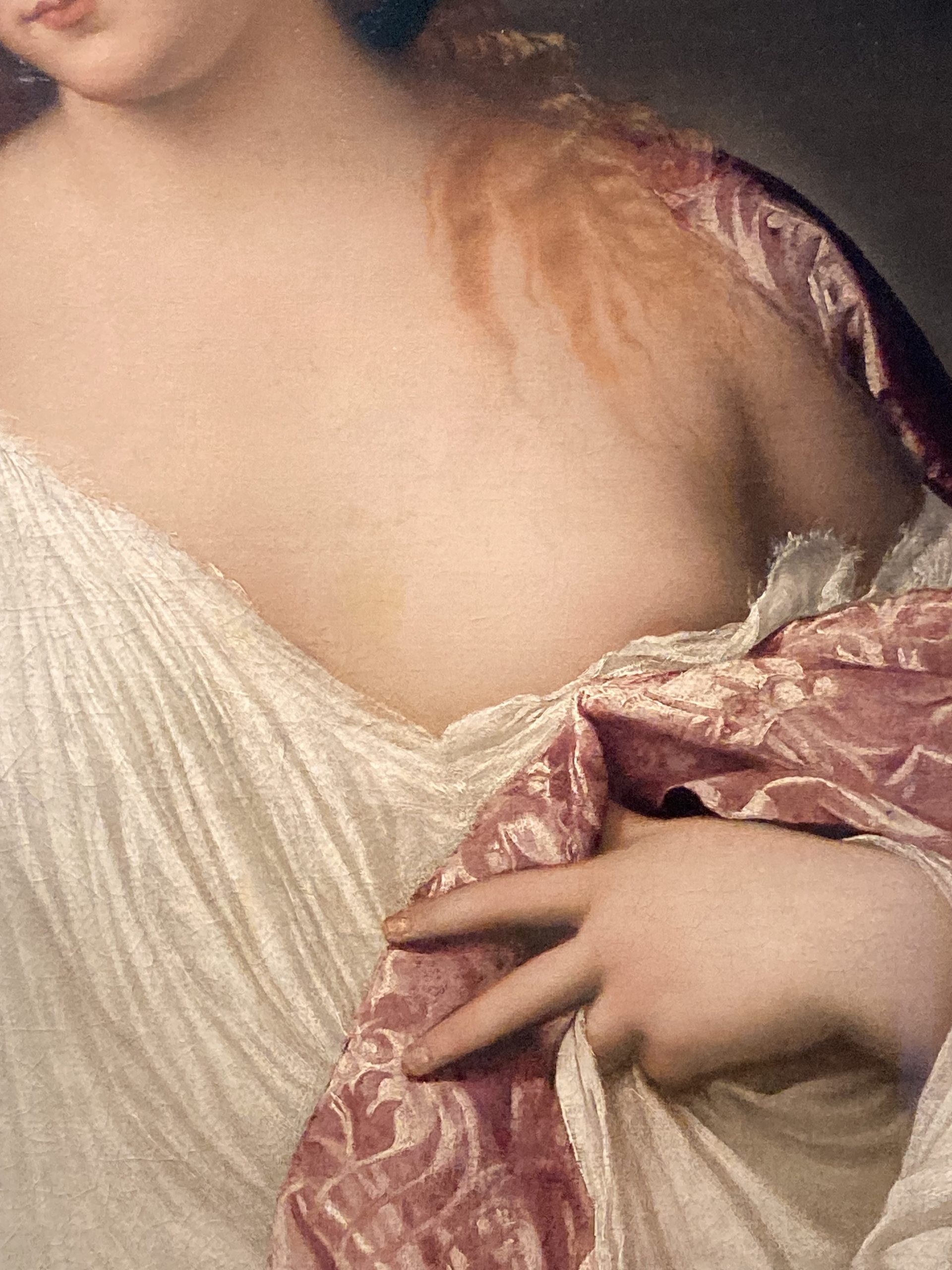 Titian’s Flora (detail: hand), a young woman with long copper-blonde hair wearing a white draped garment, holds a small bouquet of violets, rosebuds and jasmine against a dark background.
