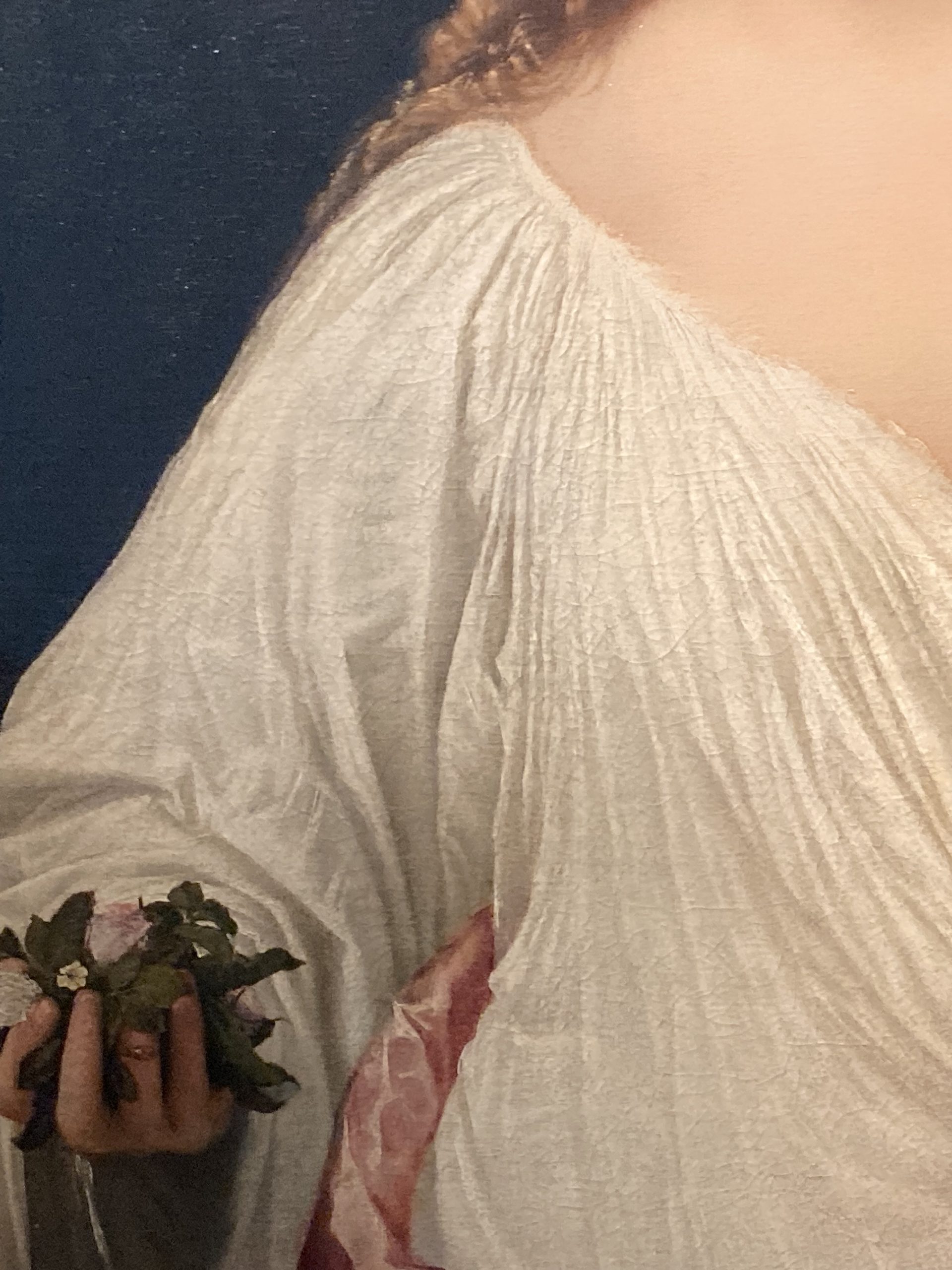 Titian’s Flora (detail: flowers ), a young woman with long copper-blonde hair wearing a white draped garment, holds a small bouquet of violets, rosebuds and jasmine against a dark background.
